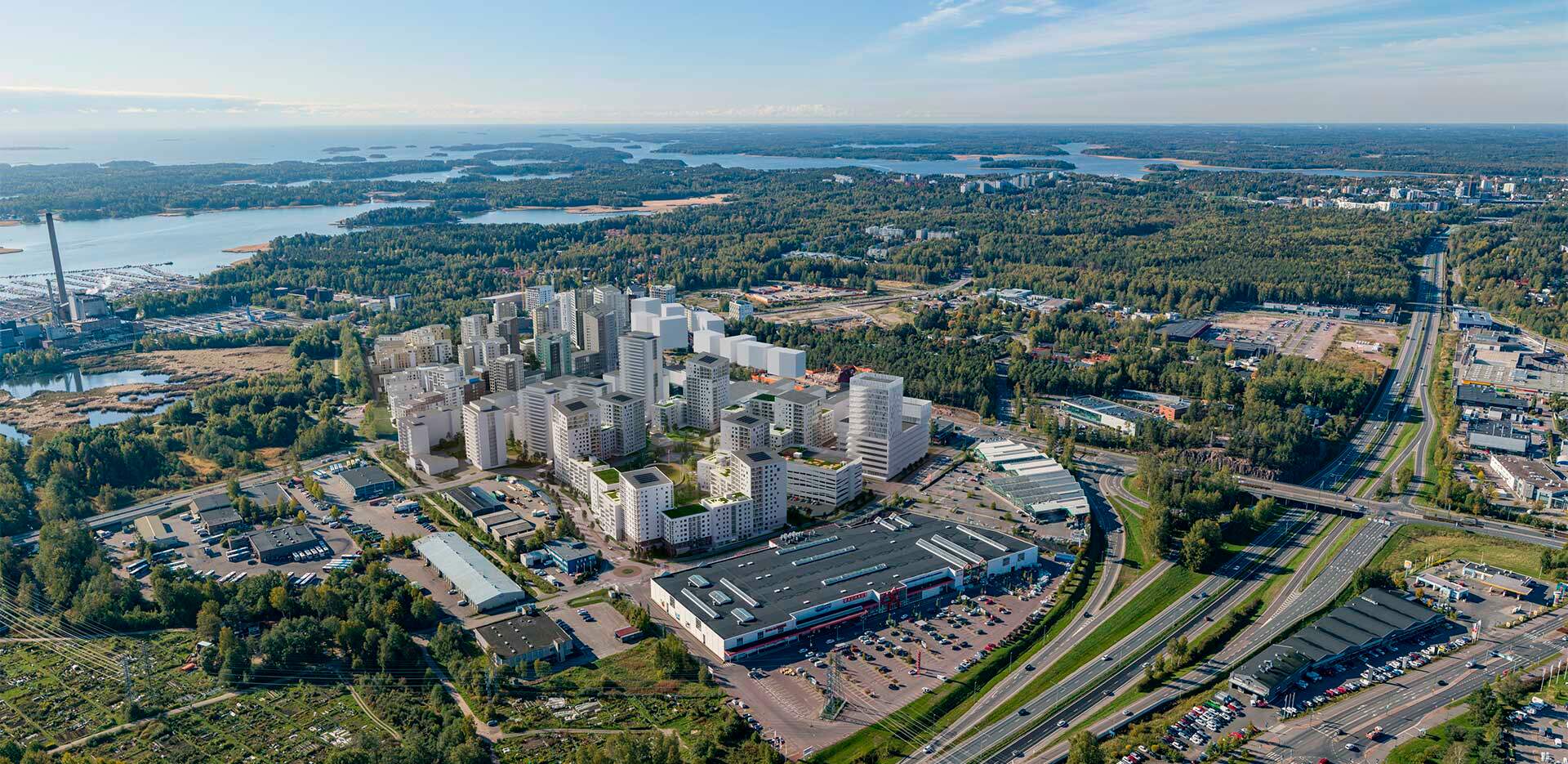 Visualisointi - Ilmakuva kaupunginosasta, jossa näkyy uusia kerrostaloja, teollisuusalue, vesistö ja metsää. Taustalla kulkee moottoritie.