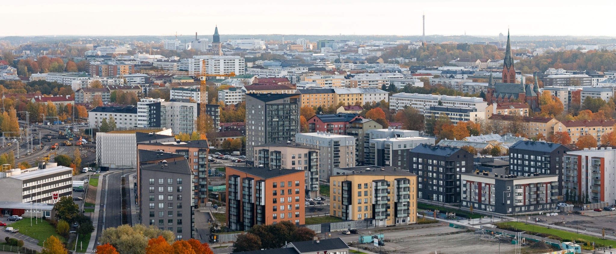 Ilmakuva Turun Kirstinpuiston alueesta. Kuvassa näkyy uusia kerrostaloja, rakennustyömaita ja kaupungin siluetti, mukaan lukien kirkontorni. Syksyinen maisema, jossa rakennukset ja puut hehkuvat lämpimissä sävyissä.